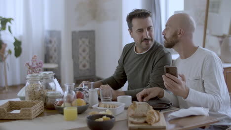 homosexual couple looking at phone screen while having breakfast