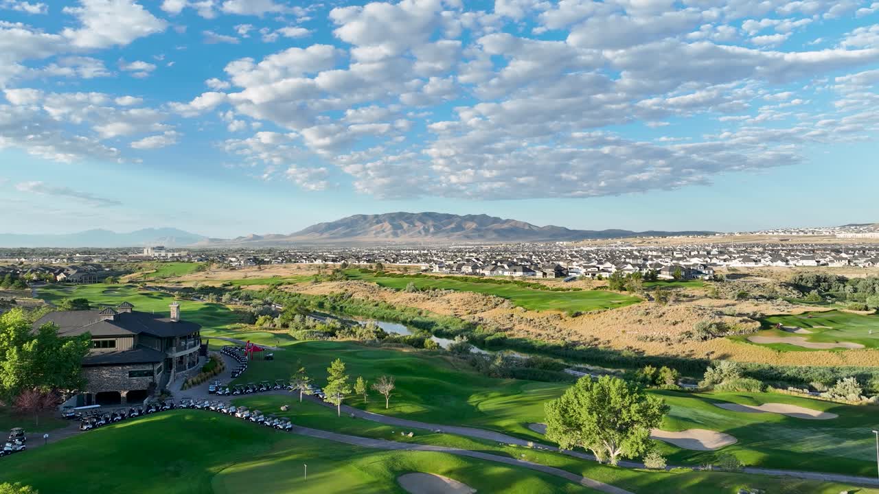 From Draper, Utah - forward aerial view over a golf course, canal, and towards the Timber Ridge neighborhood in the Salt Lake Valley along the Wasatch Front on a partly clouds sunny morning