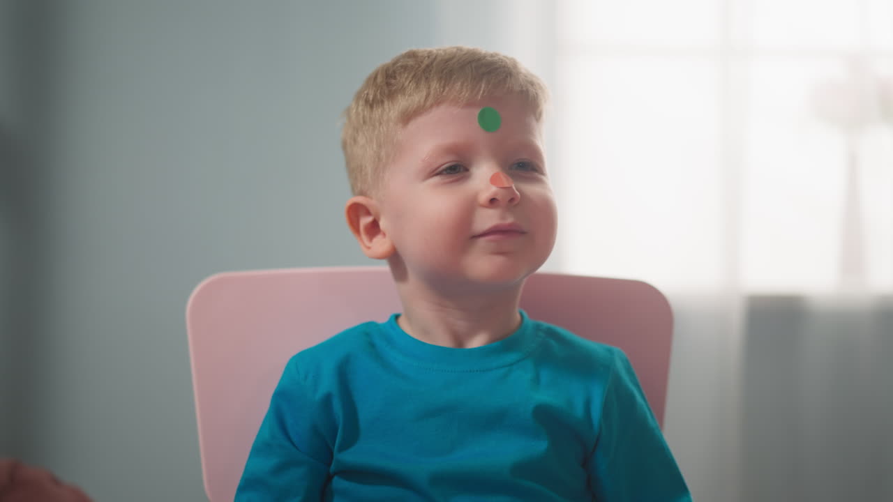 Mano di bambina incolla adesivi a pois sul naso del bambino, a casa, in primo piano.