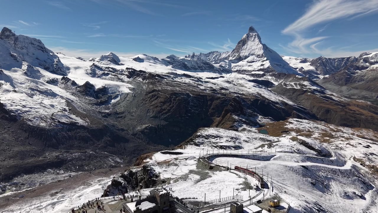 Sorvolo aereo sull'osservatorio di Gornergrat a Zermatt, Svizzera, con vista sul Cervino e un treno che scende lungo la ferrovia in una nevosa giornata autunnale nelle Alpi svizzere.