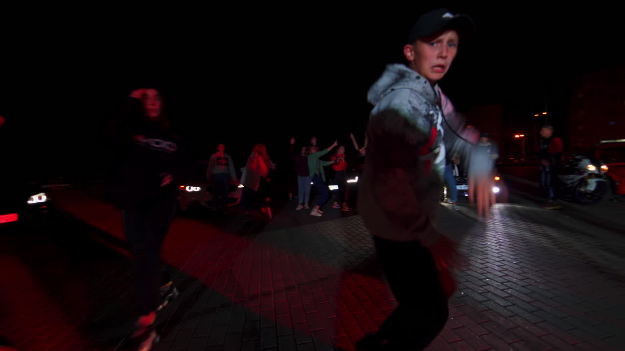 Teenagers dancing hip hop at dark time of the day. Young people having pastime dancing. Race cars at backdrop.