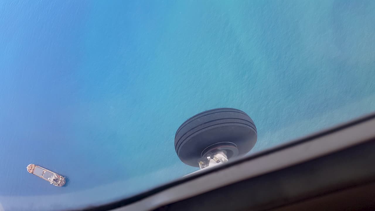 vista mirando por la ventana de un pequeño avión en la rueda del tren de aterrizaje, agua azul turquesa verde del océano y volando sobre un gran barco cisterna de carga de contenedores en los trópicos remotos del sudeste asiático