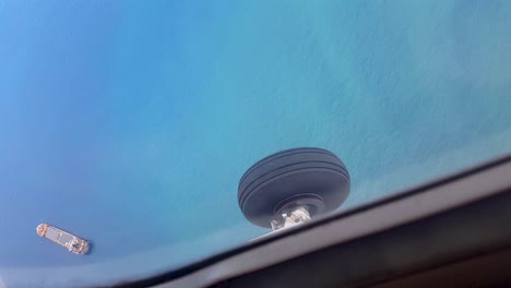 View-looking-out-of-window-of-small-plane-at-landing-gear-wheel,-turquoise-blue-green-ocean-water-and-flying-over-large-shipping-container-cargo-tanker-boat-in-the-remote-tropics-of-Southeast-Asia