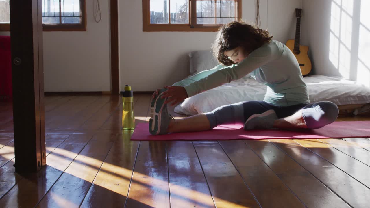 mujer de raza mixta sana haciendo ejercicio, sentada y estirándose en el dormitorio de la cabaña