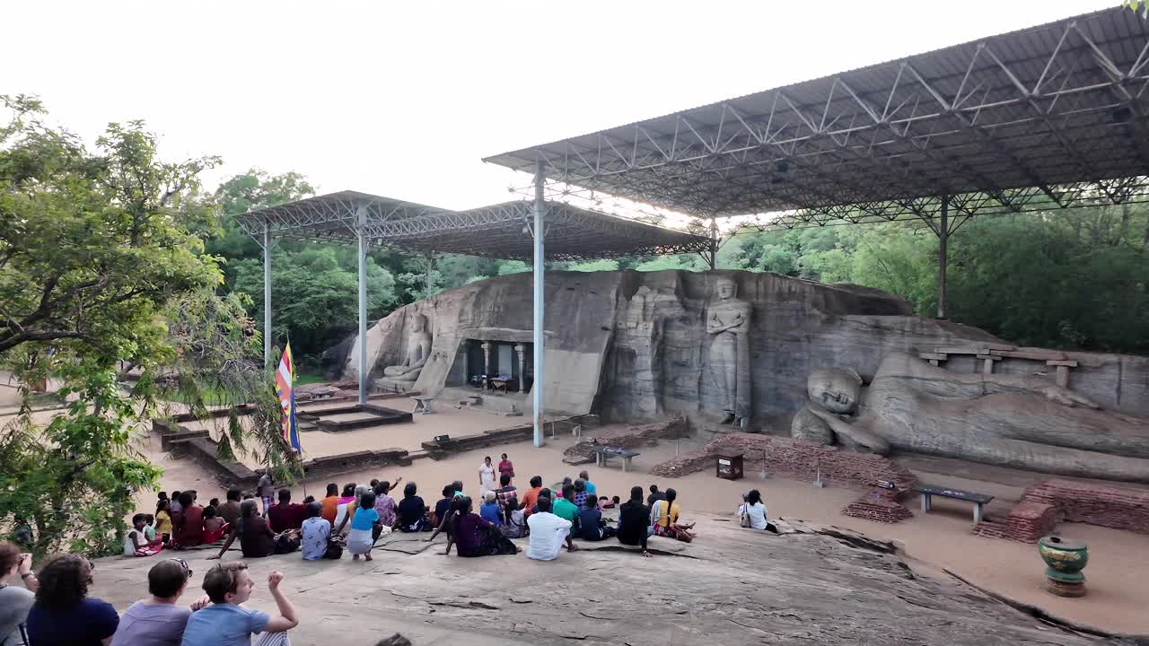 Tourists sitting on a rock, admiring the gal vihara, a rock temple with four buddha statues carved into it, located in polonnaruwa, sri lanka
