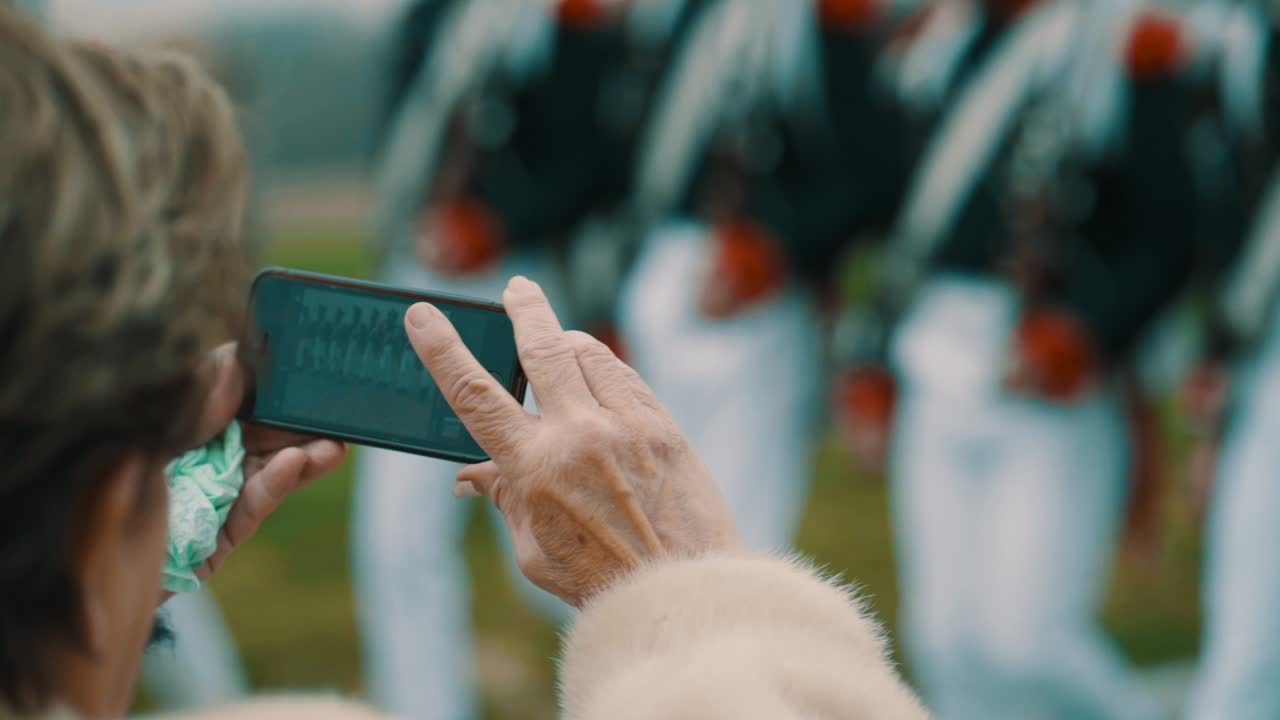 Taking a picture with the smartphone of marching soldiers in beautiful uniform in slow motion.
