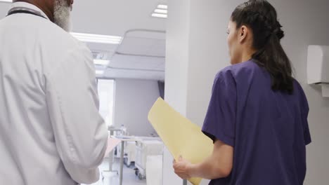 Diverse-male-and-female-doctors-holding-clipboard-and-tablet,-talking-at-hospital