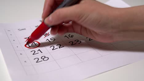 la chica tacha los días del calendario y hace círculos el 14 de febrero, día de san valentín.