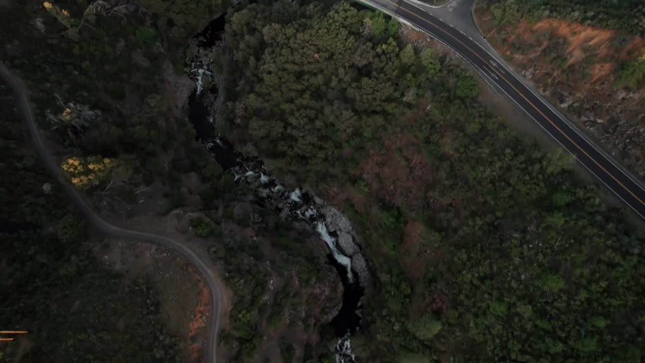 Aerial drone shot over river water flowing through green vegetation covered mountain range with long bridge Natural landscape