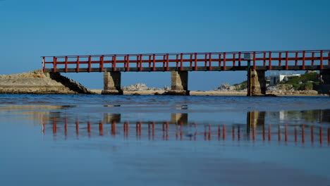 red bridge over lagoon reflected in wet sand, kleinmond, south africa