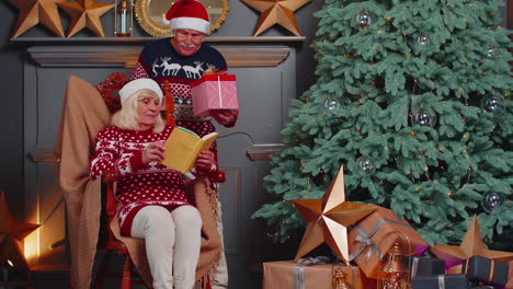 la abuela mayor presenta una caja de regalos de navidad al abuelo sorprendido mientras lee el libro