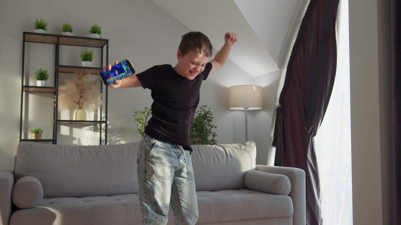 Young boy joyfully dances in living room holding smartphone enjoying music and movement the cheerful