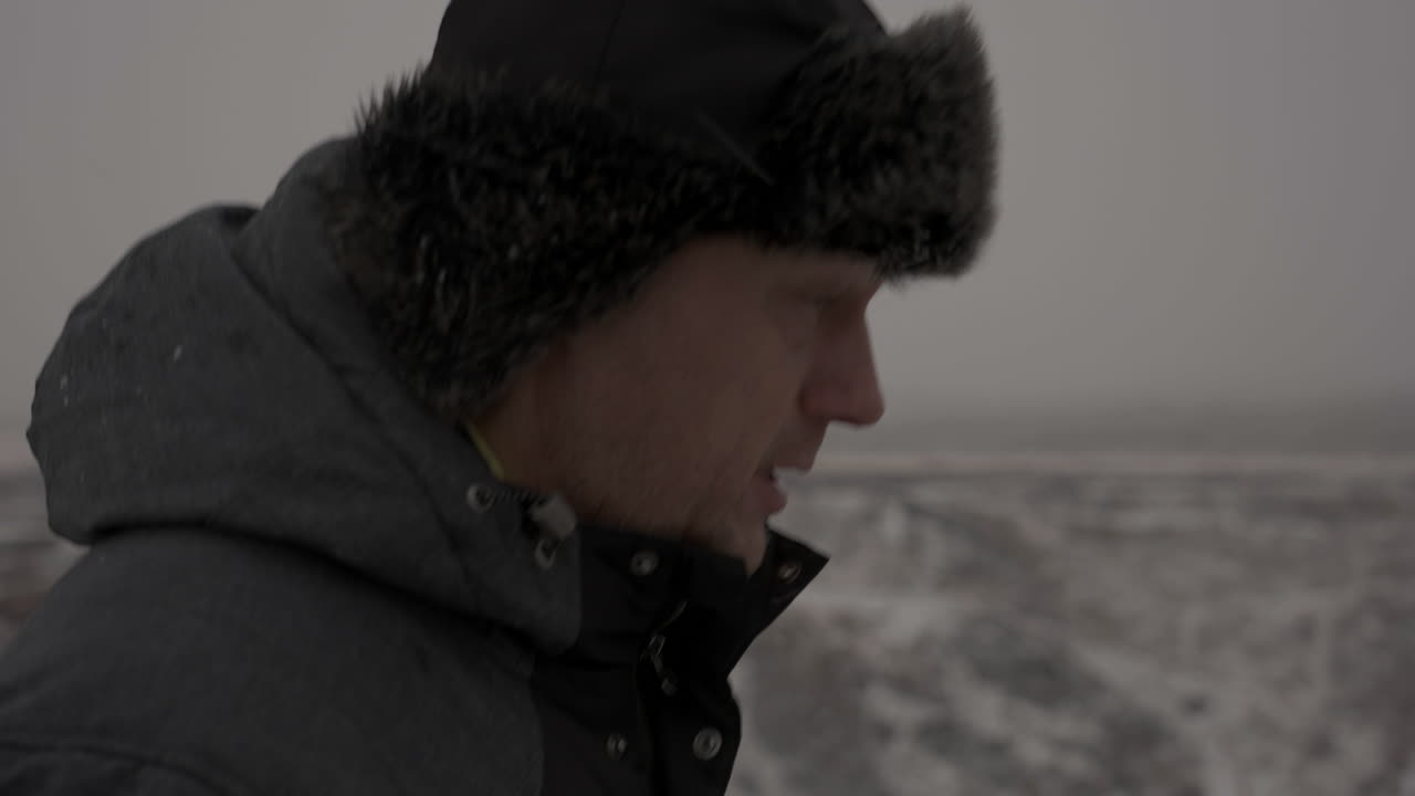 따뜻한 재킷과 겨울 모자를 쓴 중년 남성의 프로필이 추운 풍경 속에서 걷고 있습니다.