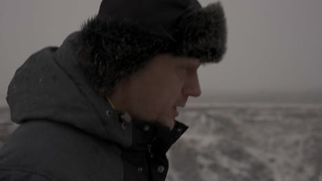 Profile-of-Middle-Age-Man-in-Warm-Jacket-and-Winter-Cap-Walking-in-Cold-Landscape,-Close-Up