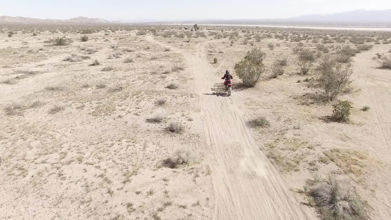 AEREA: Un motociclista da cross entra rapidamente nell'inquadratura e si allontana con la sua moto Honda CRF nel deserto.