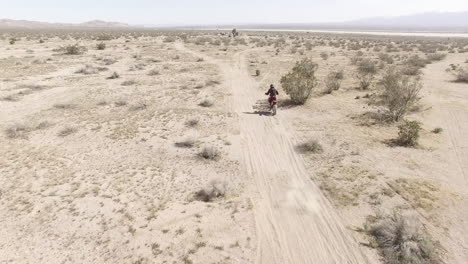 aerial: a dirt biker comes into frame quickly and rides away on his honda crf motorcycle into the desert