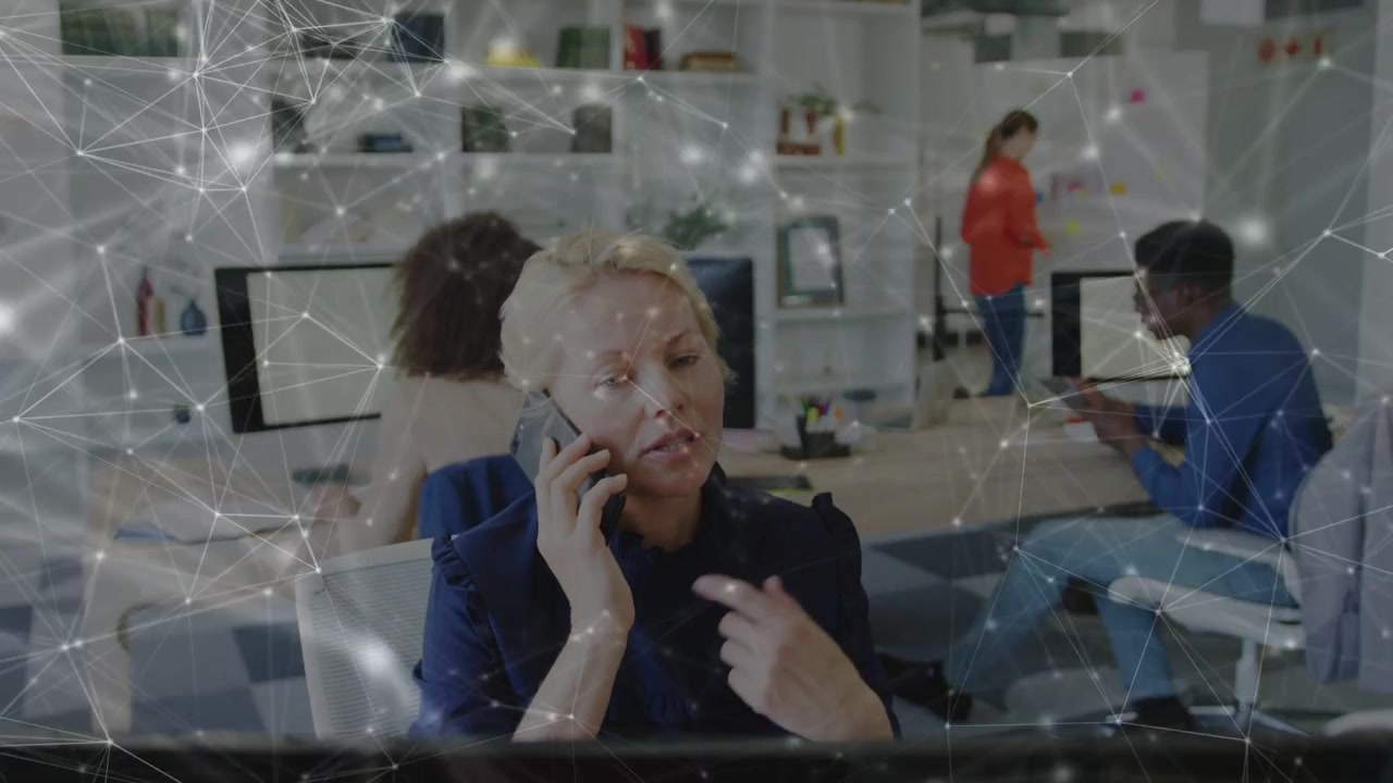 Blonde woman answering phone in open office, coordinating team while network graphic linking tablet