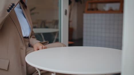 las manos de la mujer de negocios sosteniendo una taza con capuchino caliente en una pequeña mesa de café de cerca