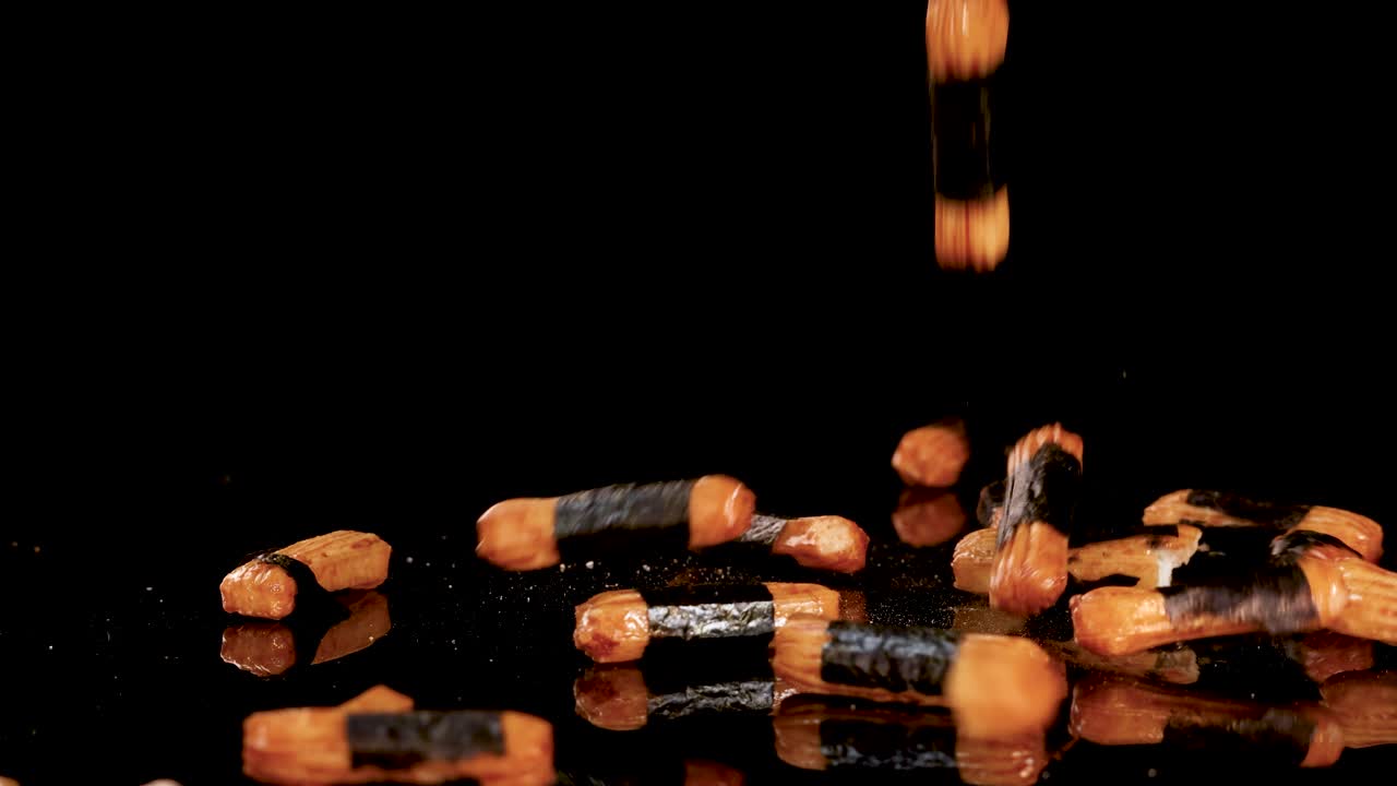 Crispy Japanese rice crackers drop and scatter, illuminated dramatically against a glossy black background