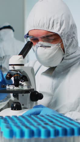 vertical video: biological scientist in coverall using microscope doing research