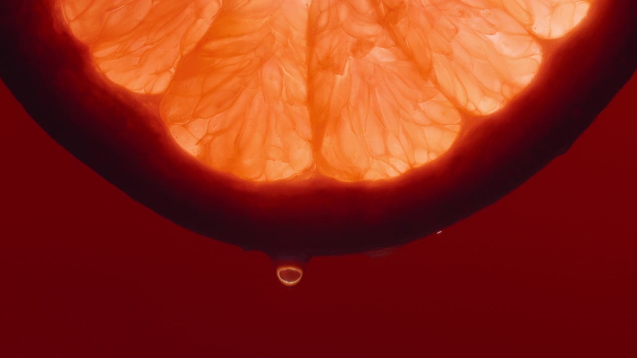 Makrobild på en vattendroppe som faller från en grapefruktskiva på röd bakgrund