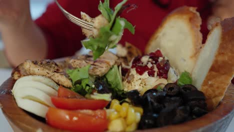 Close-up-side-view-of-woman-eating-grilled-chicken-salad-from-wooden-bowl