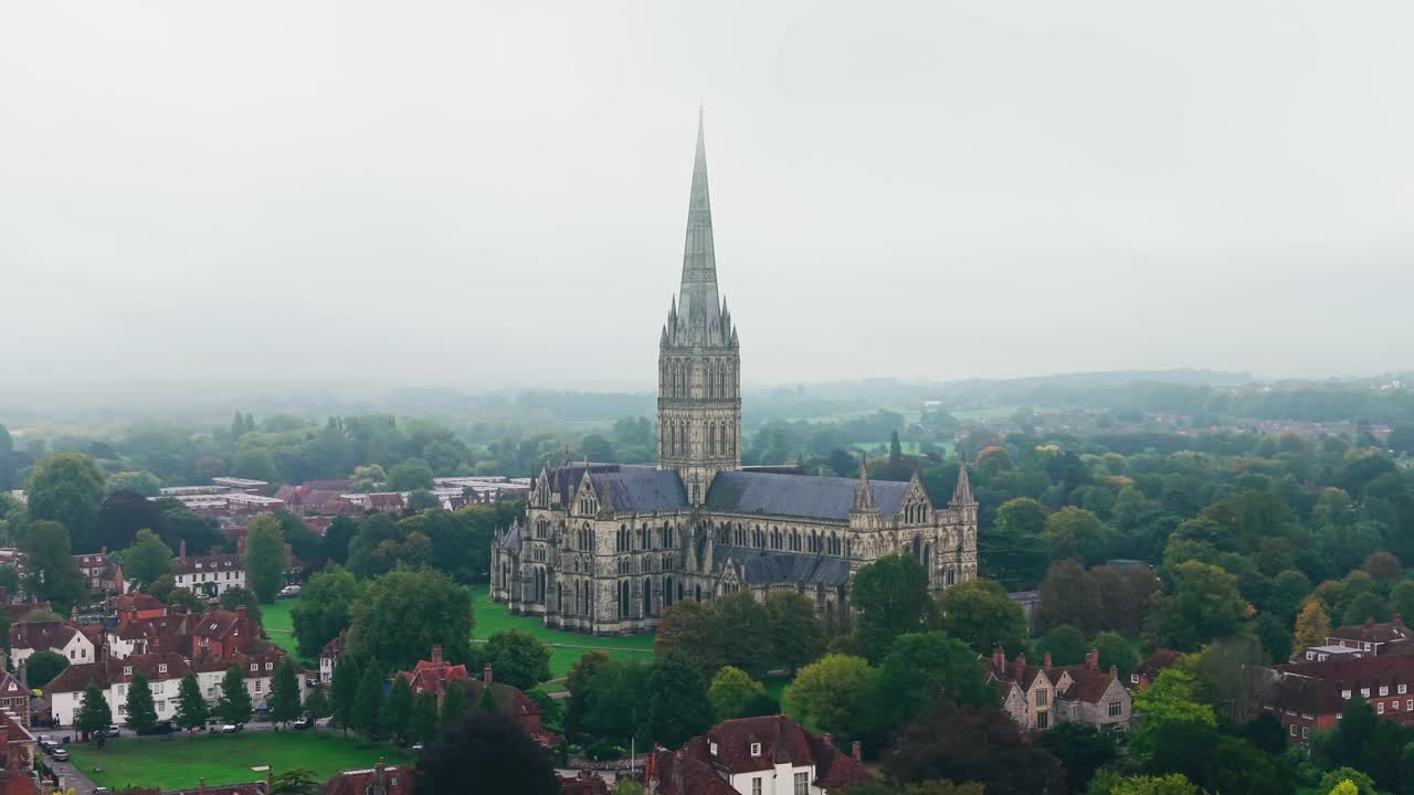Droneoptagelse af Salisbury Katedral omgivet af den historiske by Salisbury i Wiltshire, England. Det berømte katedralspir rejser sig over traditionelle engelske huse og grønt landskab