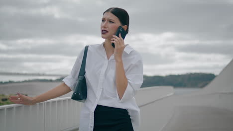 Businesswoman-dissatisfied-phone-conversation-standing-outdoors-cloudy-day.