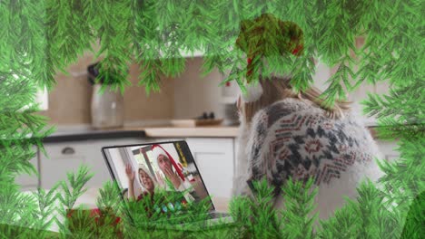 ramas verdes sobre una mujer caucásica con sombrero de santa haciendo una videollamada en una computadora portátil durante la navidad