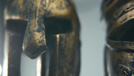 a close-up macro detailed shot of a spartan design, two different ancient warrior metal bronze helmets, glowing textured face mask shapes, studio lighting, 4k cinematic video, slow motion, pan right