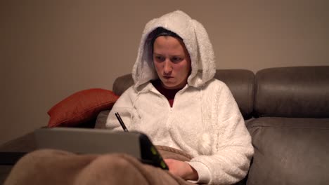 young woman dressed in bunny pajamas uses tablet and writes