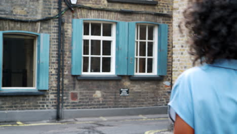 Trendy-young-black-woman-in-blue-shirt-dress-and-sunglasses-walking-on-the-street,-turning-to-camera,-back-view