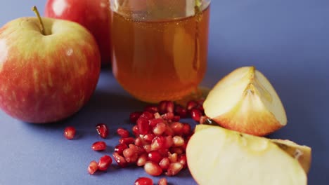 video de miel en frasco, arándanos, manzanas y rodajas de manzana sobre una superficie azul