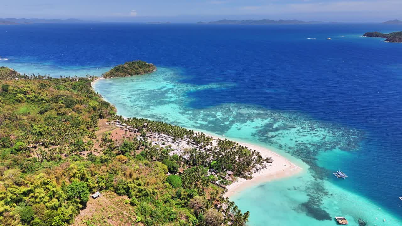 Curved white-sand beach and dense Cocos nucifera palm cover of Darocotan Island, nestled in the Sulu Sea off northeastern Palawan, Philippines, known for its reefs and coastal serenity, drone descend
