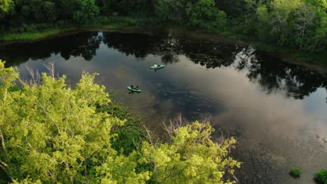 aerial drone tilt down orbit over pair of kayaking fisherman on clear, still river water at sunrise