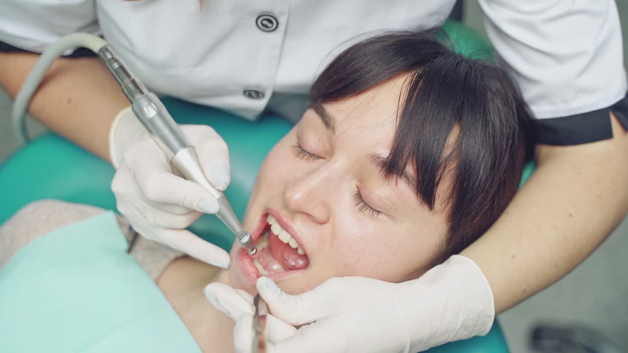 Young woman on the procedure of removing deposits on the teeth. A dentist uses special tool for a cleaning . Close-up.