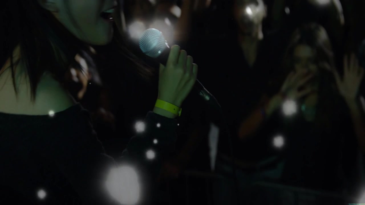 Singer moving through music club to engage fans, audience lighting phones, bokeh drifting over mic