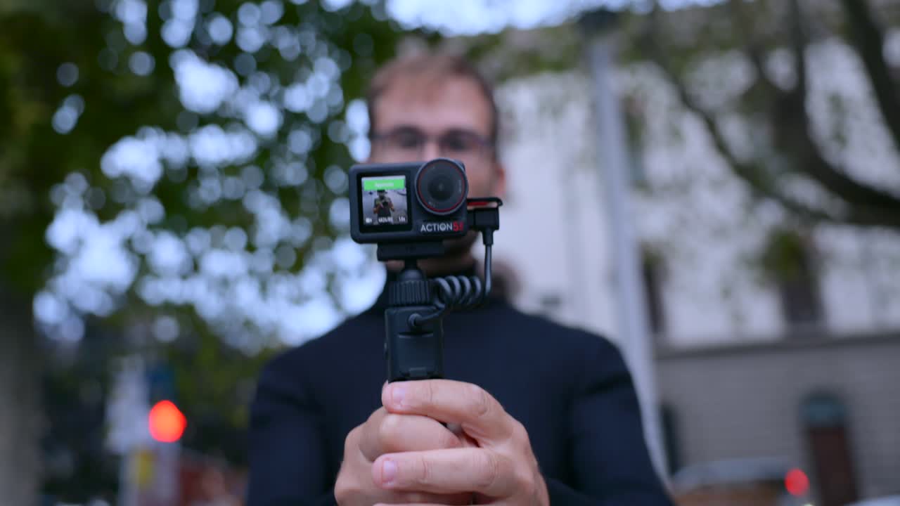 Closeup of man using gymbal with mounted action camera outside, streets