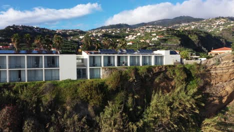 un hombre joven y en forma con cabello largo y barba estirando los brazos en el aire, alcanzando el cielo con emoción y alegría desde su balcón del hotel en la cima del acantilado de ponta do sol en madeira