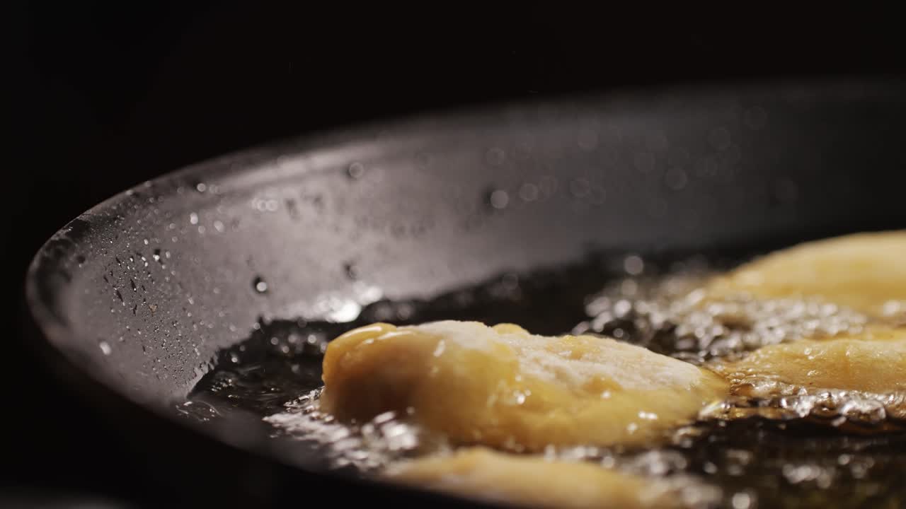 American chiken nuggets broiling on black frying pan close-up macro. Breaded nagget of chiken meat. Man cooking fast food. High quality 4k footage
