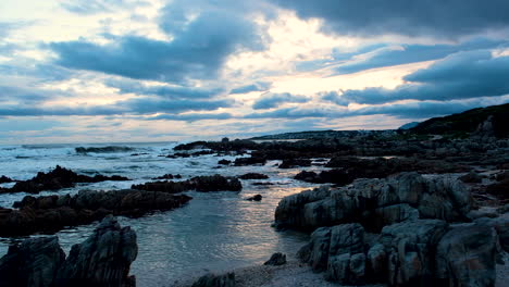 Vibrant-moody-cloudscape-at-sunset-over-rocky-coastline,-trucking-over-beach