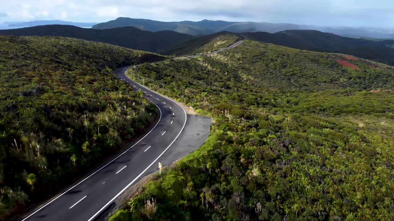 Drone view of an empty winding road in between forest on a sunny day in Cape Reigna, Northland, New Zealand.