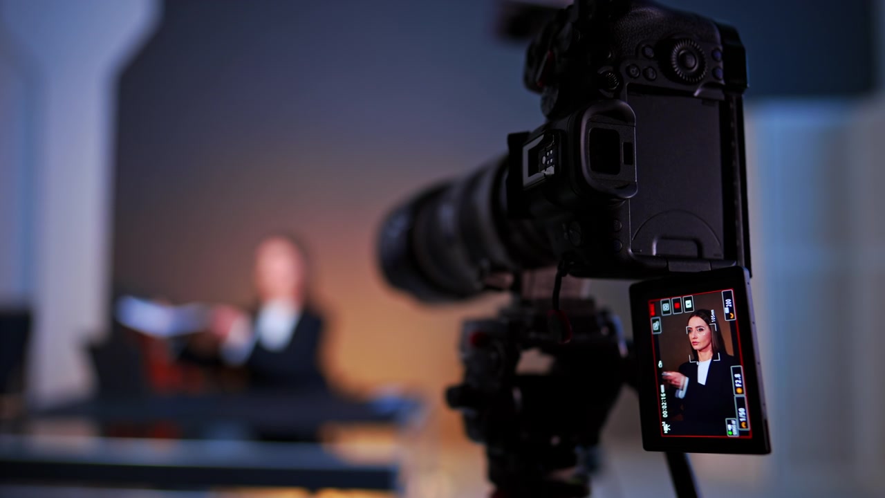 Monitor LCD della telecamera che mostra una donna durante le riprese di un'intervista video. Primo piano del retro di una telecamera professionale con schermo ribaltabile che mostra una donna seduta a una scrivania in studio