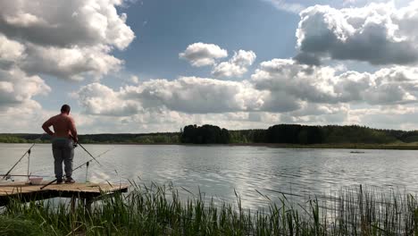 Man-fish-with-fishing-rod-from-edge-of-wooden-pier-during-bright-cloudy-day