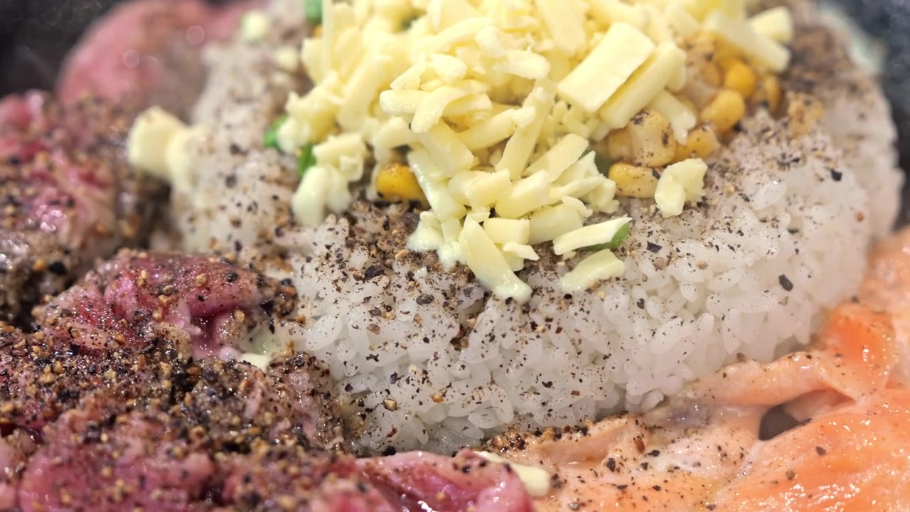 Riso caldo in padella condito con maiale tenero, salmone e formaggio fuso, creando un piatto ricco e saporito con una combinazione soddisfacente di consistenze e sapori