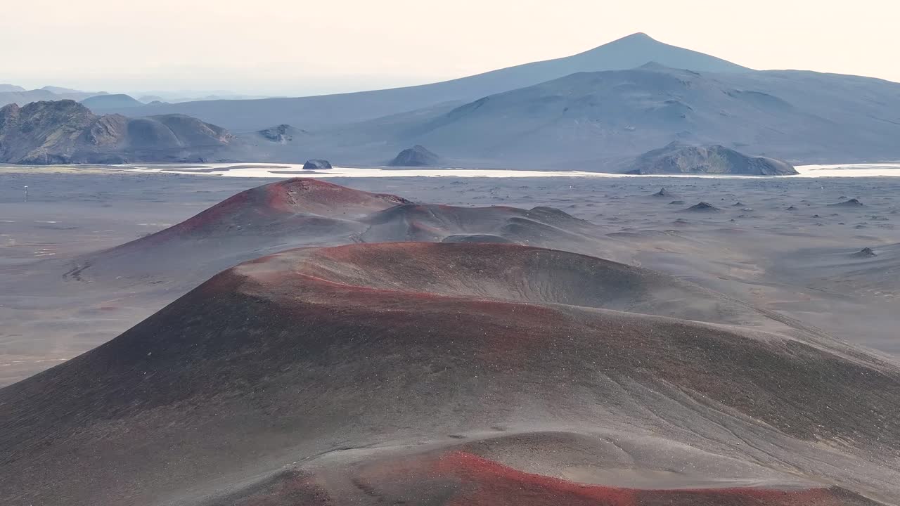 Flying low over the open mouths of three red volcanic crater in the highlands of Iceland on a clear day in summer