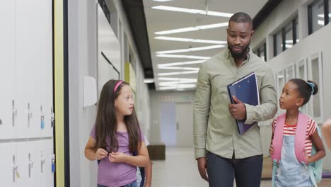 Video-of-happy-african-american-male-teacher-and-diverse-female-pupils-walking-at-school-hall