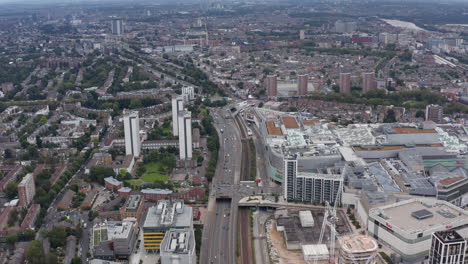 High-angle-view-of-modern-complex-with-tall-residential-buildings-and-huge-shopping-mall.-Tilt-up-revealing-cityscape.-London,-UK