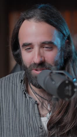 man with long hair and beard smiling and speaking into a microphone