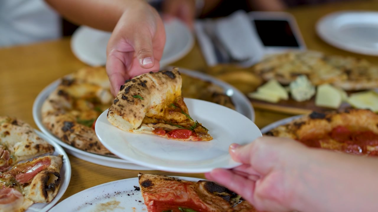 Beyaz bir tabağa taze bir pizza dilimi servis eden bir elin yakın çekimi.